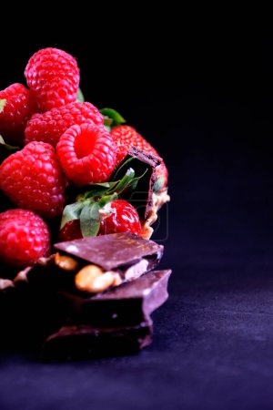 Fresas y frambuesas con trozos de chocolate en una taza de gofre sobre un fondo negro