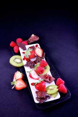 Plato de frutas. Fresas, frambuesas, kiwi y trozos de chocolate en un plato rectangular.