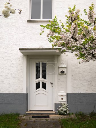 Foto de La puerta delantera blanca entre los árboles florecientes - Imagen libre de derechos