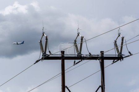 Substation power grid pointing upward with commercial airplane flying in the sky.