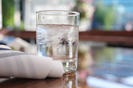 sobre una mesa de madera un vaso de agua limpia con hielo y una servilleta blanca