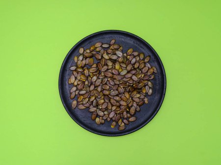 Pumpkin seeds on a black wooden plate on a green background