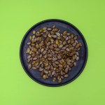 pumpkin seeds on a black wooden plate on a green background