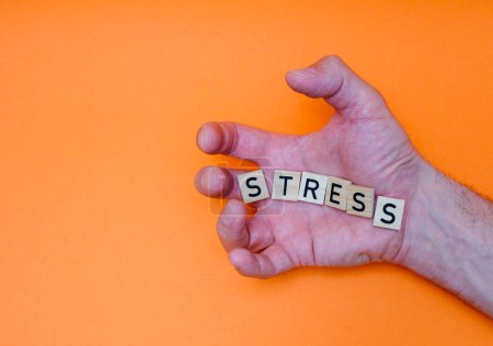 das Wort STRESS ist aus Holzbuchstaben auf der Handfläche mit gelähmten Fingern ausgelegt