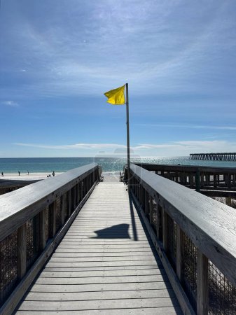 Public walkway with yellow beach flag flying and view of Navarre Beach fishing pier 