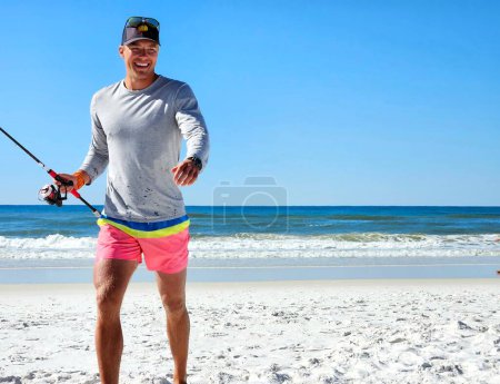 Young millennial man walking on beach in summertime with smile on his face.
