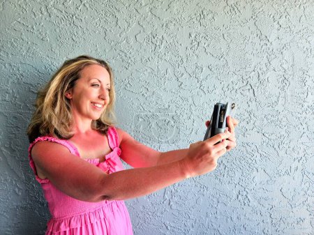 Young millennial lady in pink taking a selfie on blue background. 