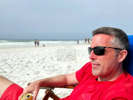 Cooler Mann der Generation X in Schattierungen trinkt Bier und entspannt am Strand.