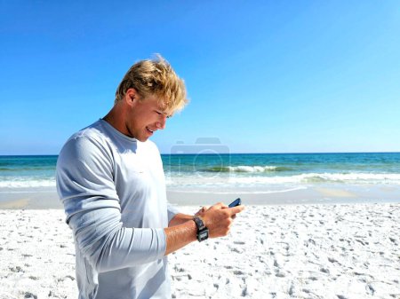 Junger Mann am Strand SMS auf Handy im Profil. 