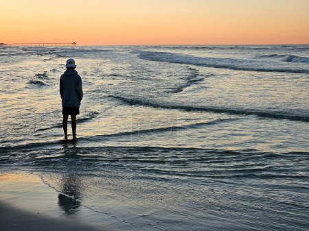 Silhouette Tourist steht in der Brandung des Meeres und beobachtet den Sonnenaufgang im Urlaub. 