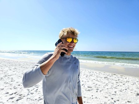 Happy millennial guy using cellphone on sandy beach in Florida to communicate. 
