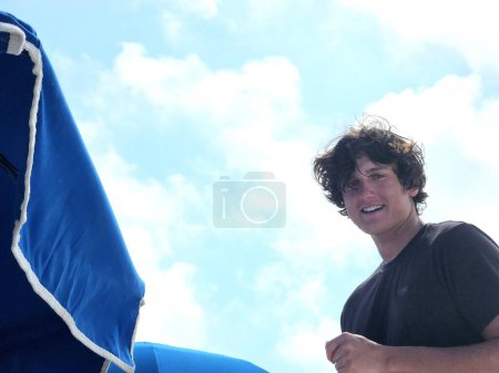 Hombre joven Millennial trabajando en la playa en verano la creación de sombrillas y sillas de playa. 