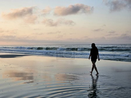Silhouette Frau im Urlaub spazieren am Strand bei Sonnenaufgang im Sommer. 