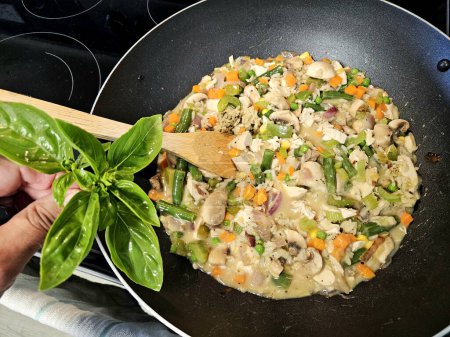Adding basil herbs to stir fry chicken and rice in a wok.