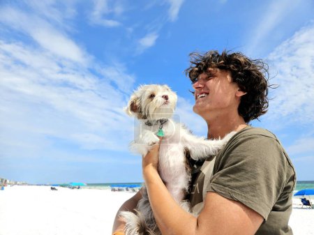 Young man Millennial plays with cute dog on beach in summertime. 