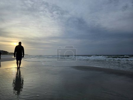 Silhouetted tourist man walking down beach on foggy morning in Florida. 