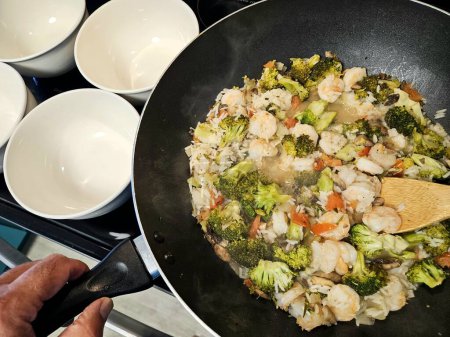 Overhead food flat lay shrimp and broccoli sauted with rice and vegetables in a wok stovetop. 
