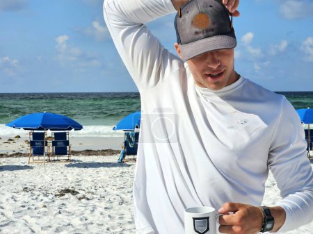 Young millennial man at Florida beach drinking coffee on vacation in white sweatshirt. 