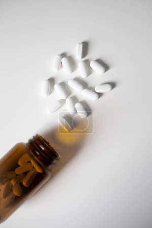 White pills spilled from glass bottle on white background