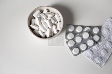 Pilules blanches dans un bol et plaquettes thermoformées sur fond blanc