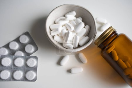 Weiße Pillen aus Glasflasche verschüttet, in Schale und Blasen Tabletten auf weiß gesammelt