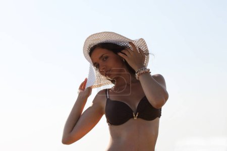 Junge gebräunte Frau posiert in Badebekleidung und Strandhut