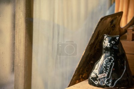 A ceramic feline companion, holding a cigarette in its hand, rests gracefully beside a sunlit window, adding charm to the artistic atmosphere of the painting studio