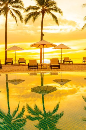 Téléchargez les photos : Parapluie et chaise autour de la piscine dans la station hôtelière avec lever du soleil le matin - concept vacances et vacances - en image libre de droit