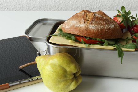 Gesunde Pause: Umweltfreundliche Lunchbox mit Roggen-Sandwich, Obst und digitalen Geräten