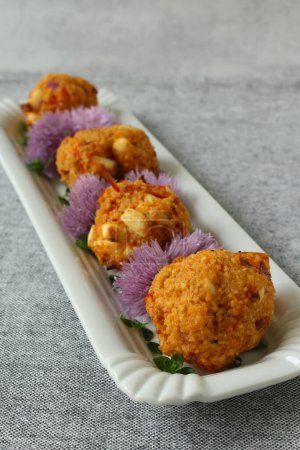 Couscous-Feta-Kugeln mit Schnittlauch-Blüten auf neutralem grauen Hintergrund