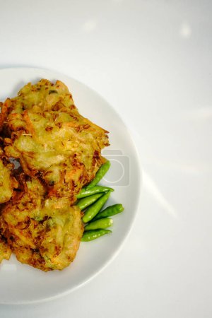 Selective focus Bakwan sayur or Bakwan Goreng or bala-bala or ote-ote is vegetebles fritter from Indonesia, served with cayenne peppers on white plate.