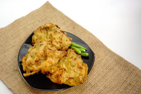 Selective focus Bakwan sayur or Bakwan Goreng or bala-bala or ote-ote is vegetebles fritter from Indonesia, served with cayenne peppers on black plate.