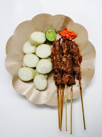 Sate Ayam (Chicken satay) with peanut sauce and lontong (rice cake). One of the popular street food in Indonesia. Selective focus.