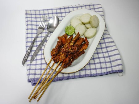 Sate Ayam (Chicken Satay) mit Erdnusssoße und Lontong (Reiskuchen). Eines der beliebtesten Streetfood Indonesiens. Serviert in weißem Teller auf weißem Tisch. Selektiver Fokus.