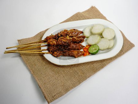 Sate Ayam (Chicken Satay) mit Erdnusssoße und Lontong (Reiskuchen). Eines der beliebtesten Streetfood Indonesiens. Serviert in weißem Teller auf weißem Tisch. Selektiver Fokus.
