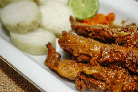 Nahaufnahme von Sate Ayam (Chicken Satay) mit Erdnusssoße und Lontong (Reiskuchen). Eines der beliebtesten Streetfood Indonesiens. Serviert in weißem Teller auf weißem Tisch. Selektiver Fokus.