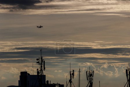 Stadtlandschaft mit einem Verkehrsflugzeug, das im Sonnenuntergangshimmel zwischen Gebäuden und Antennen fliegt