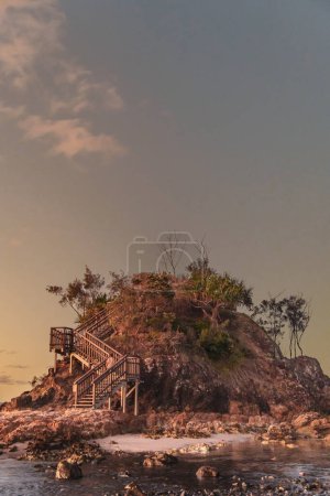 Kleine Insel inmitten des Strandes von Byron Bay in Australien, die aussieht wie die Geschichte aus dem Buch Der kleine Prinz, im rosafarbenen Licht des Sonnenuntergangs und seinen kleinen Bäumen an seiner Spitze.