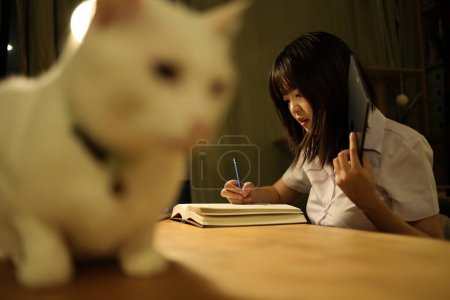 Téléchargez les photos : Une jeune étudiante en uniforme universitaire thaïlandaise est assise à un bureau pour étudier, faire ses devoirs et étudier dur. Journée internationale des étudiants, Journée mondiale des étudiants. Gén Z, E-learning - en image libre de droit