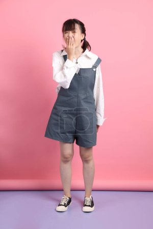 Cheerful lovely young asian woman in overalls casual clothes with gesture of Mouth close, Silent gesture isolated on pink background. St Valentine's Day, Women's Day, Birthday