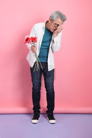 Asian senior man in casual clothing with gesture of holding a bouquet of flowers isolated on pink background. St Valentine's Day, Women's Day, Birthday