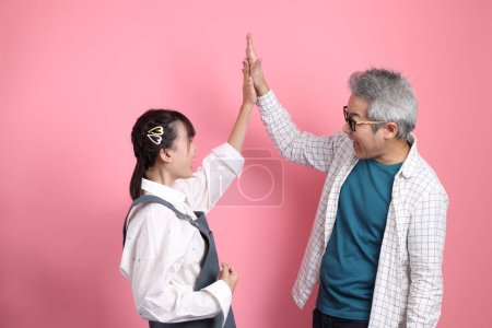 Asiatisches Seniorenpaar in Latzhosen und lässiger Kleidung mit Geste der fröhlichen, aufgeregten und feiernden Menschen auf rosa Hintergrund. Valentinstag, Frauentag, Geburtstag