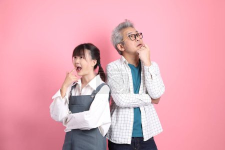 Foto de Asiático senior hombre y mujer pareja en overoles casual ropa con pensamiento aislado en rosa fondo. San Valentín, Día de la Mujer, Cumpleaños - Imagen libre de derechos
