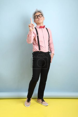 Asian senior man in black suspenders with red bow with gesture of stop, cross prohibition sign, forbid isolated on blue background. St Valentine's Day