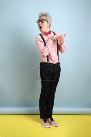 Téléchargez les photos : Homme âgé asiatique en bretelles noires avec arc rouge avec geste de prise de note et plagiat isolé sur fond bleu. Saint Valentin - en image libre de droit