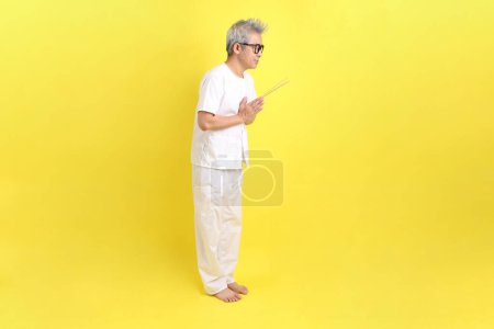 Chinese Vegetarian Festival. Senior man wearing white clothing with gesture of hand holding the incense sticks isolated on yellow background. Nine emperor god, J festival.