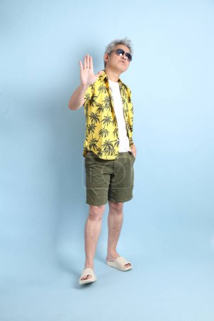 HAPPY SONGKRAN DAY. Asian tourist senior man in summer clothing with gesture of  stop, forbid, refusing isolated on blue background. Songkran festival. Thai New Year's Day.