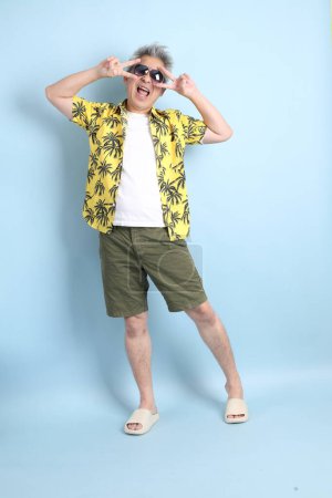 HAPPY SONGKRAN DAY. Asian tourist senior man in summer clothing with gesture of  Counting number isolated on blue background. Songkran festival. Thai New Year's Day.