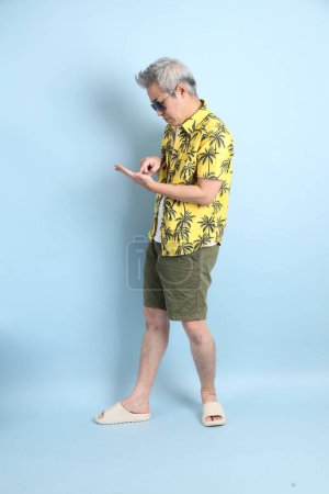 Téléchargez les photos : Heureux jour de SONGKRAN. Touriste asiatique homme âgé en vêtements d'été avec geste de prise de note et note courte isolé sur fond bleu. Festival de Songkran. Nouvel An thaïlandais. - en image libre de droit