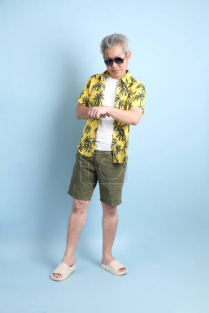 HAPPY SONGKRAN DAY. Asian tourist senior man in summer clothing with gesture of  Waiting or late isolated on blue background. Songkran festival. Thai New Year's Day.